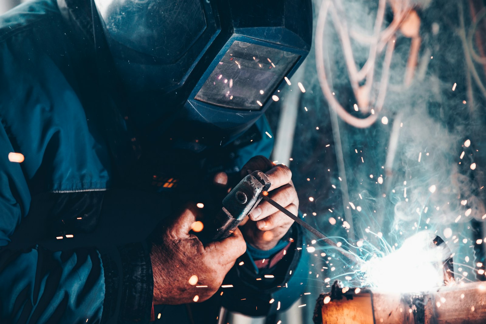 A welder in a protective mask joining steel with sparks flying.