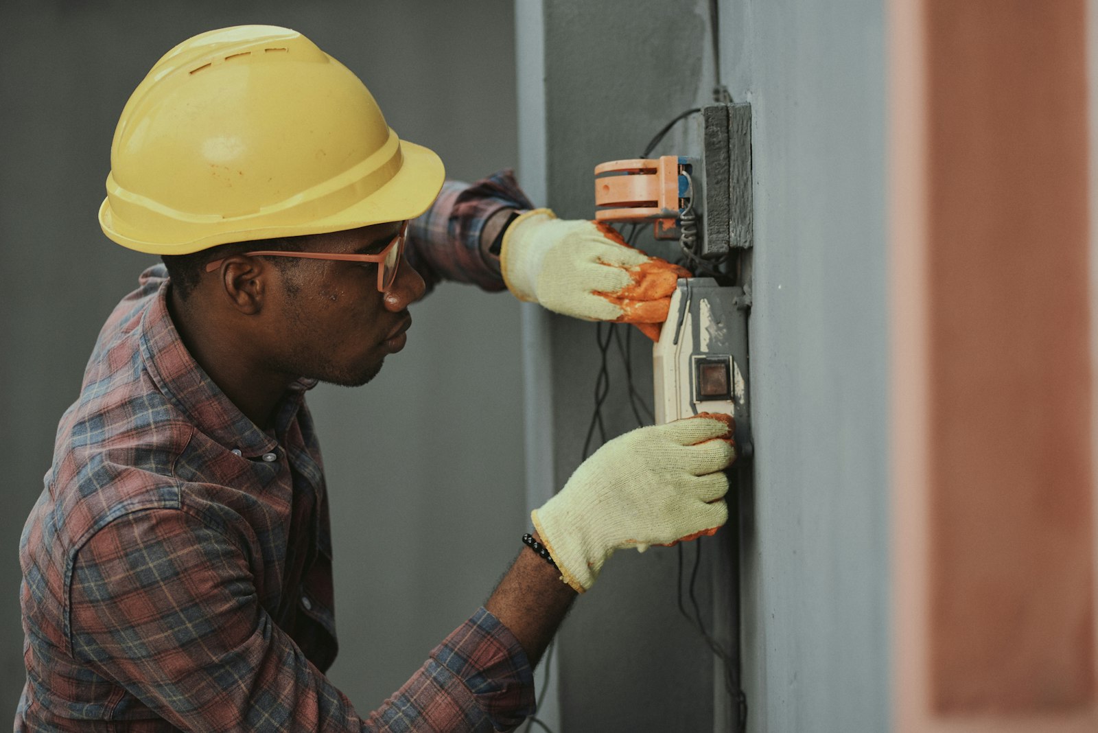 A maintenance technician in a hard hat and gloves working on an electrical panel.