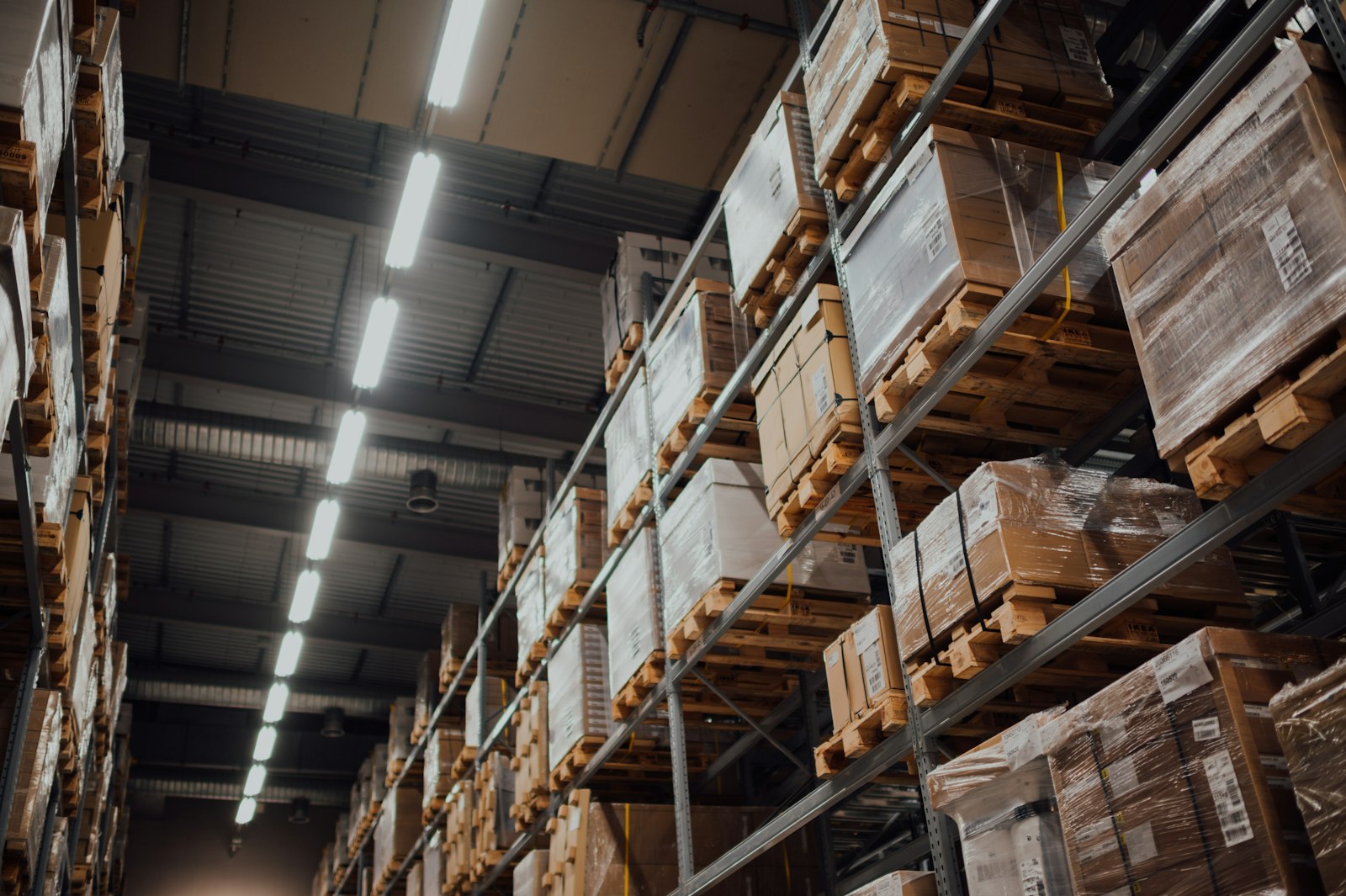 Boxed stock on high warehouse racking under strip lighting.