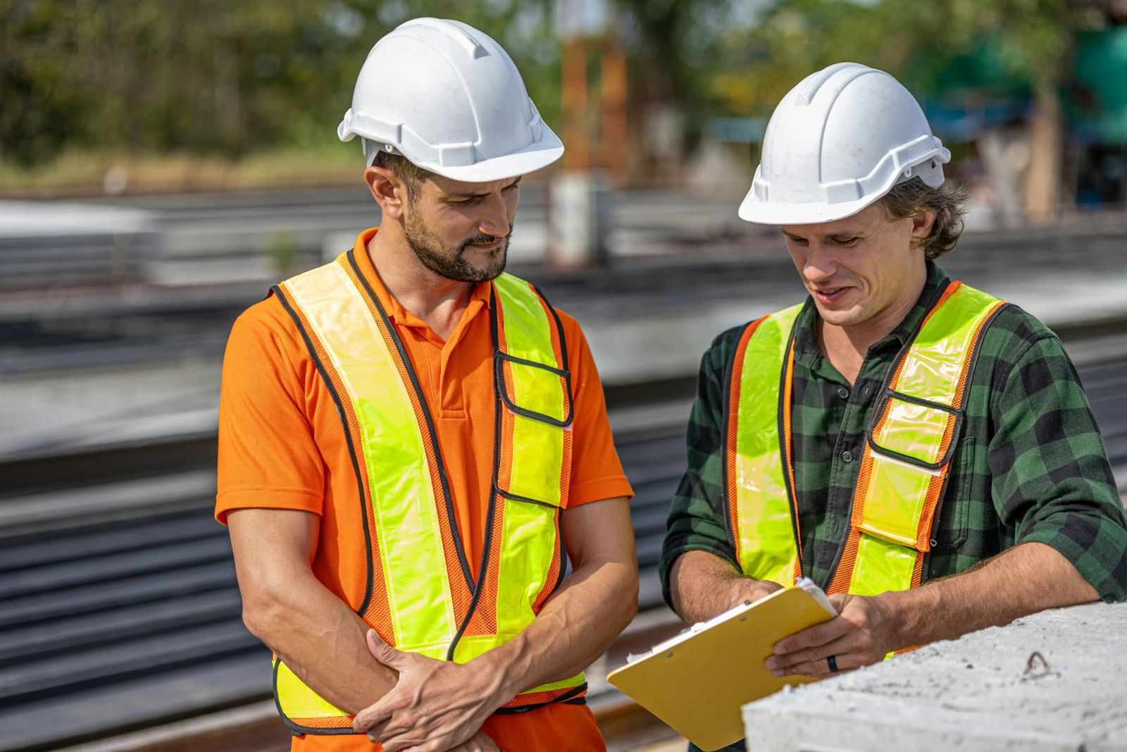 Two workers in hard hats reviewing notes on a clipboard.