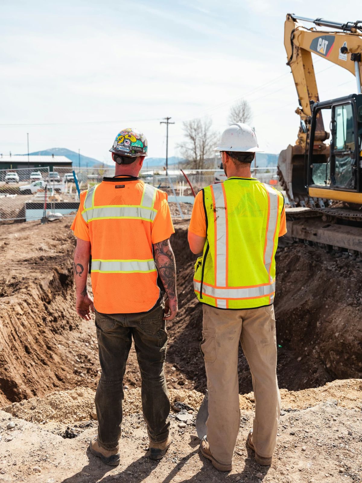 Two workers looking over an excavation beside an excavator.