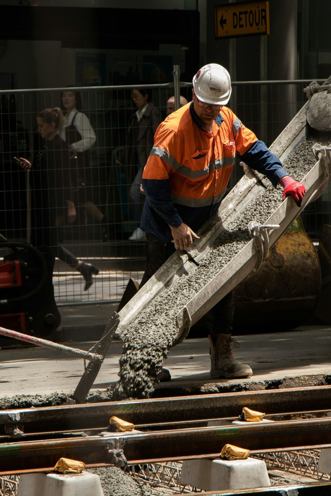 A construction worker coordinating a concrete pour beside railway tracks.