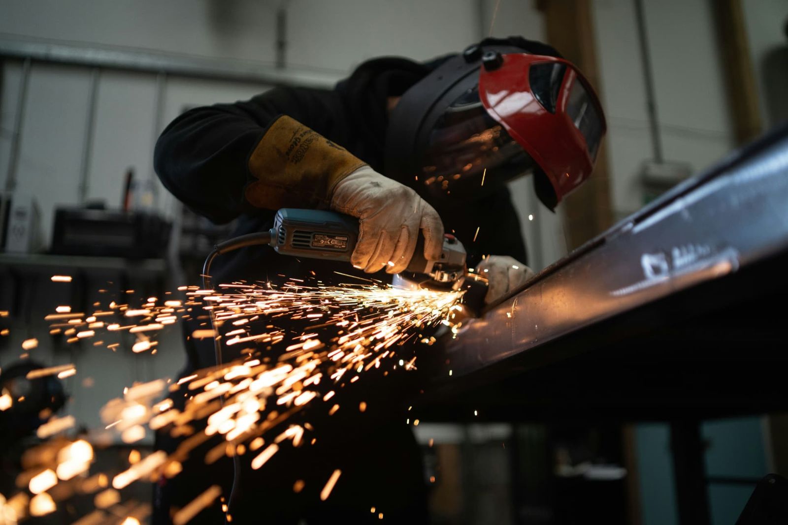 A worker wearing protective equipment grinding steel with sparks flying.